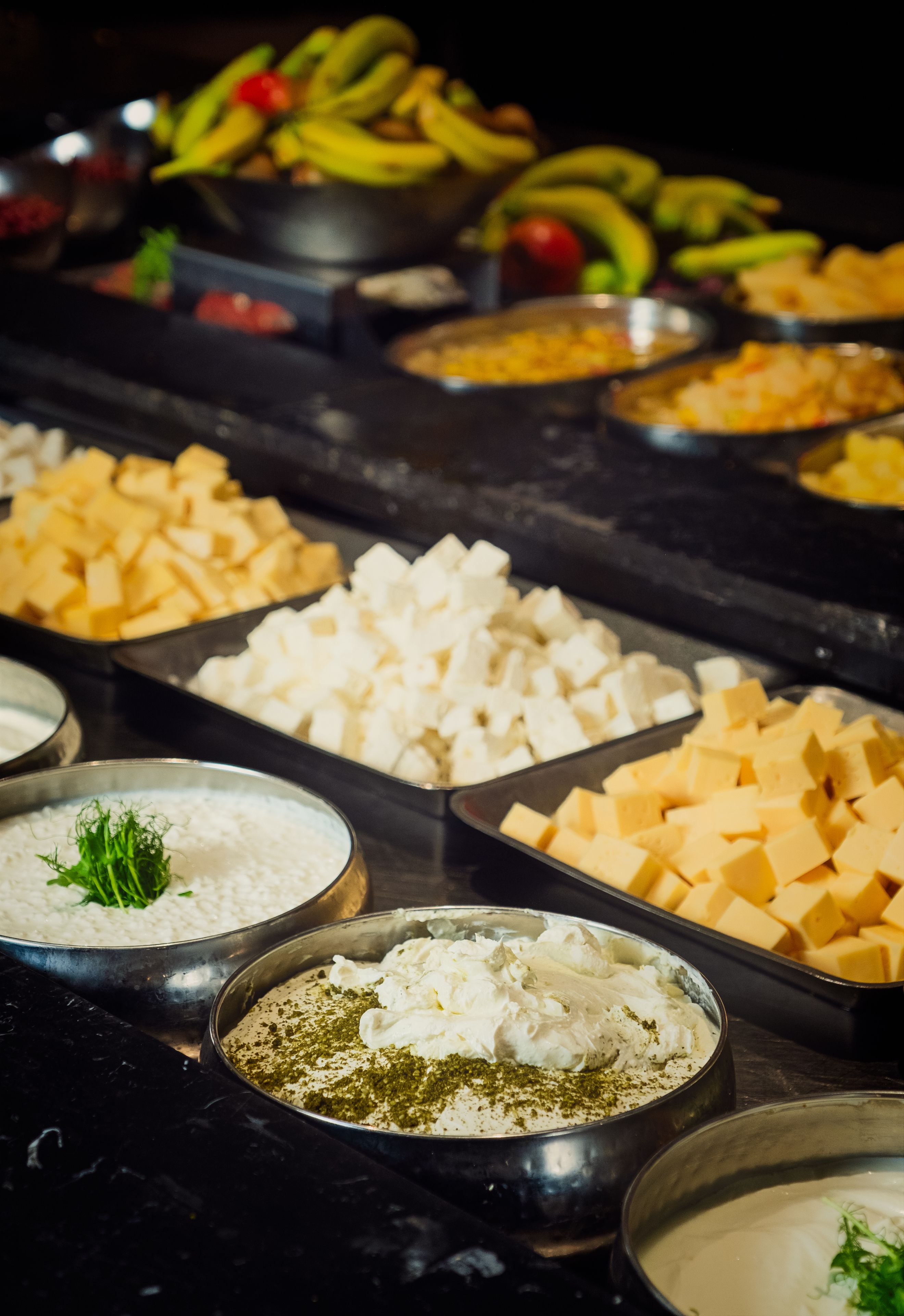 Un bufé con diversos alimentos, incluyendo queso en cubos, cubos blancos y un bol de salsa blanca adornado con hierbas.