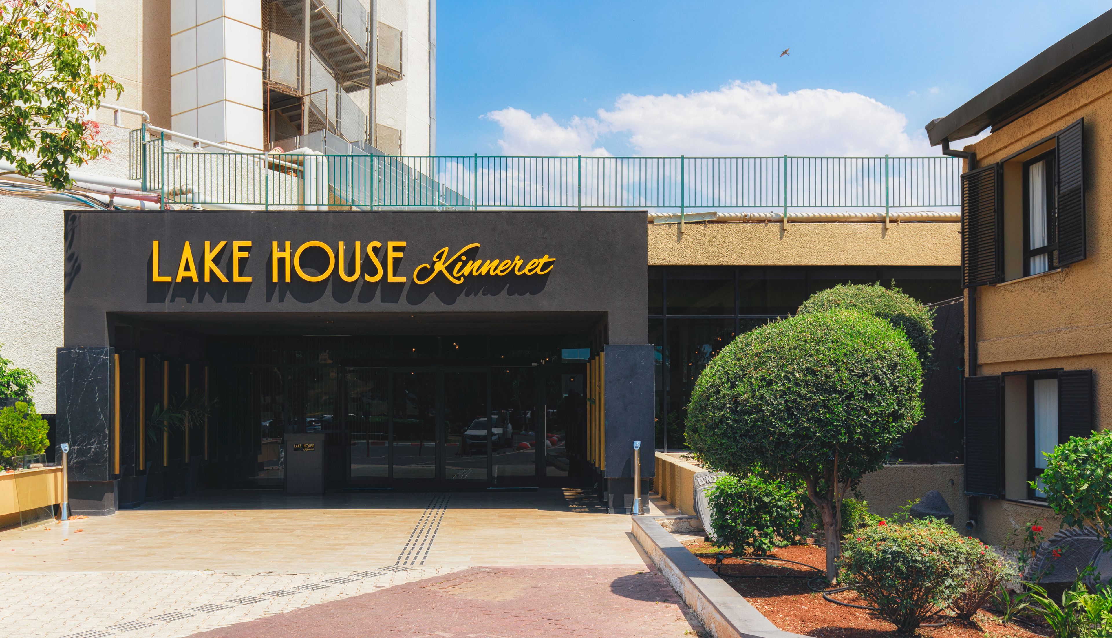 The exterior of Lake House Kinneret, featuring a modern facade, a gated entrance, and a landscaped garden area.