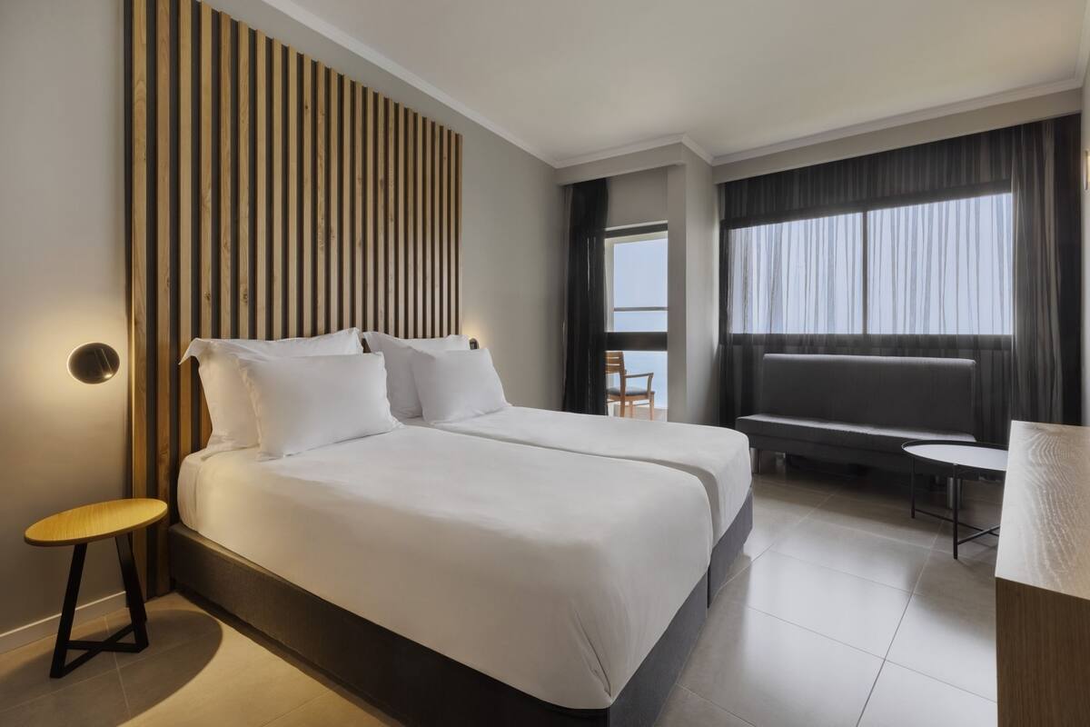 A hotel room with a large bed, a small table, a sofa, and a view of the sea.