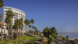 A modern hotel with a curved facade, palm trees, and a view of the ocean. - Lake House Kinneret (Tiberias)