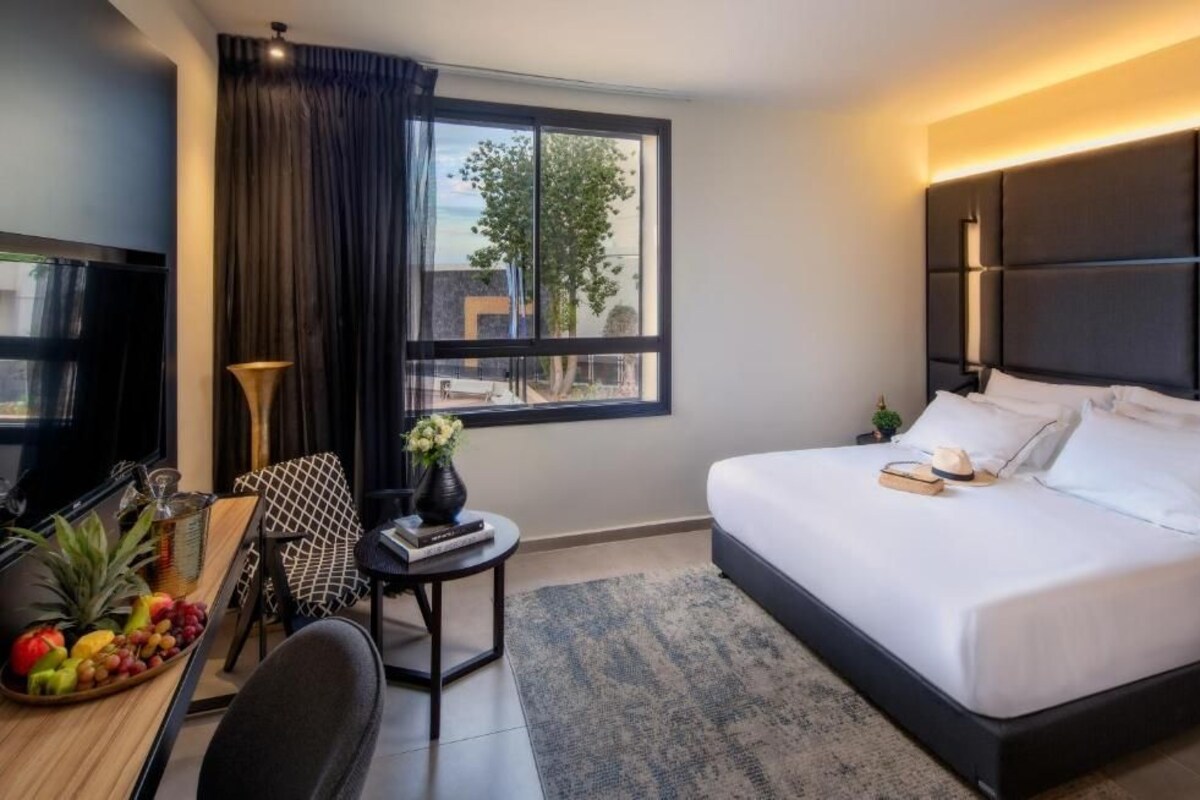 A modern hotel room with a large bed, a desk with a chair, a television, and a window with curtains.