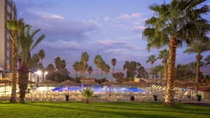 A resort pool area with lounge chairs and umbrellas, surrounded by palm trees and a view of the ocean. - Lake House Kinneret (Tiberias)