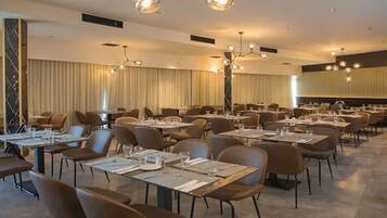 A spacious dining area with multiple tables and chairs, arranged in a modern setting with pendant lighting.