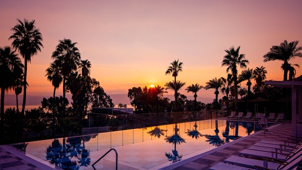 A poolside area with lounge chairs and palm trees at sunset. - Lake House Kinneret (Tiberias)