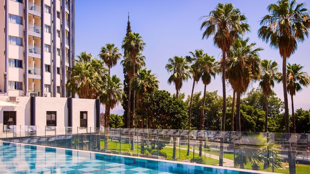 Una piscina con diseño de cuadros, rodeada de palmeras y un edificio alto con balcones.