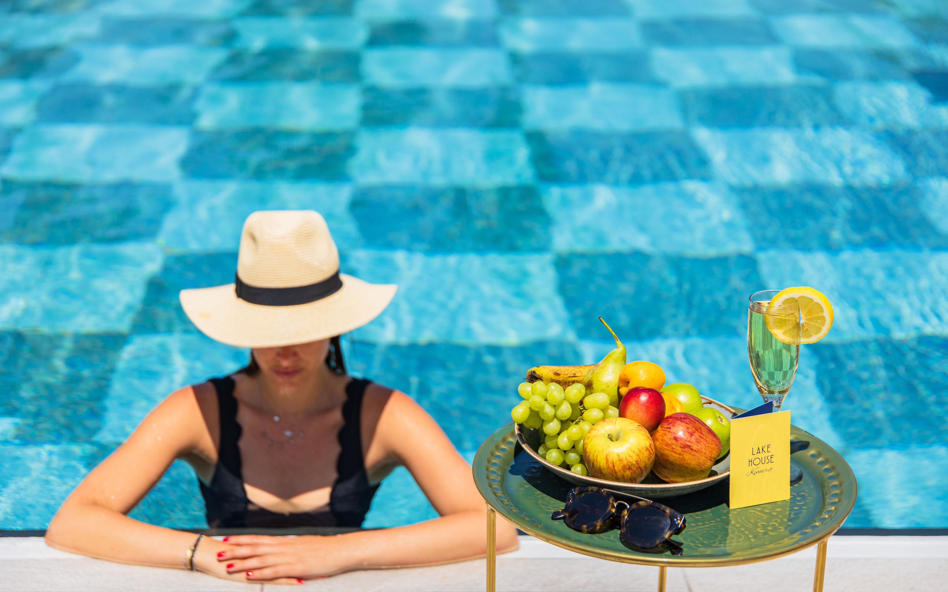 A poolside table with a fruit bowl, a glass of water, and a card labeled "LAKE HOUSE".