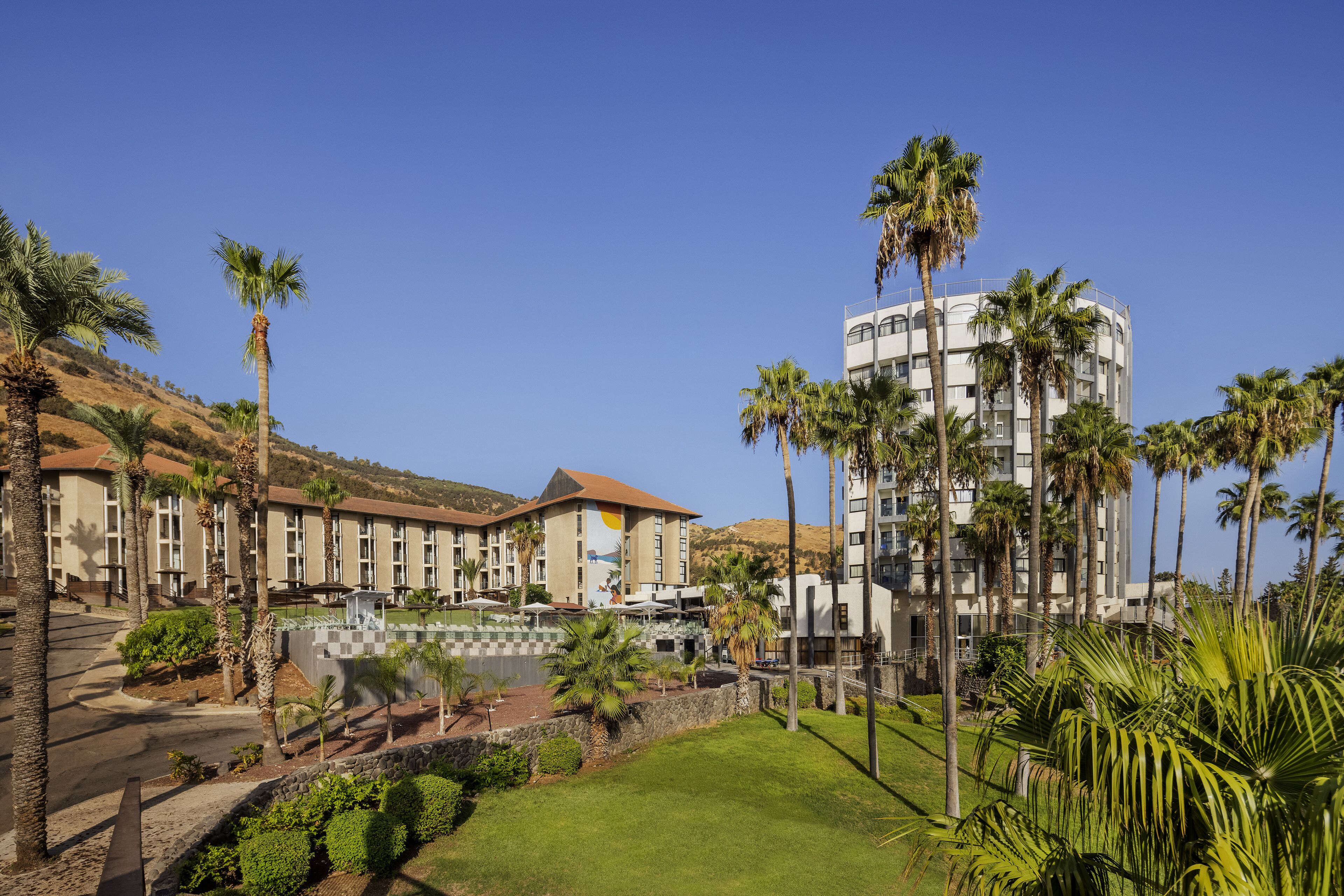 A hotel with a central courtyard, palm trees, and a mountain backdrop.