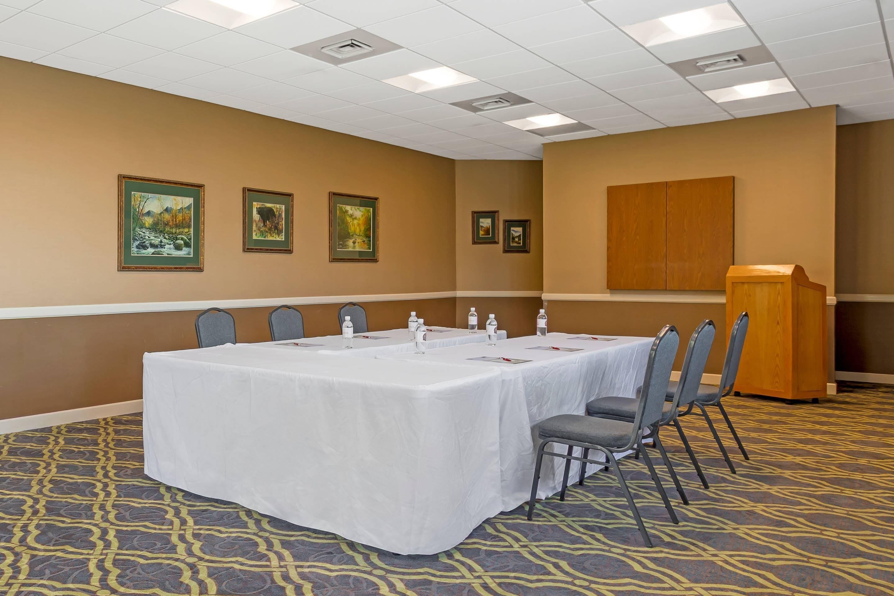 A conference room with a long table, chairs, a podium, and framed pictures on the wall.