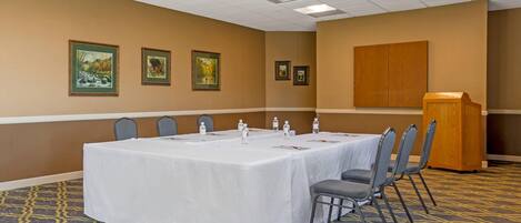 A conference room with a long table, chairs, a podium, and framed pictures on the wall.