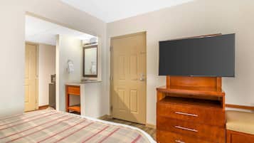 A hotel room with a bed, a television on a wooden stand, a wardrobe, a bathroom with a mirror, and a door.