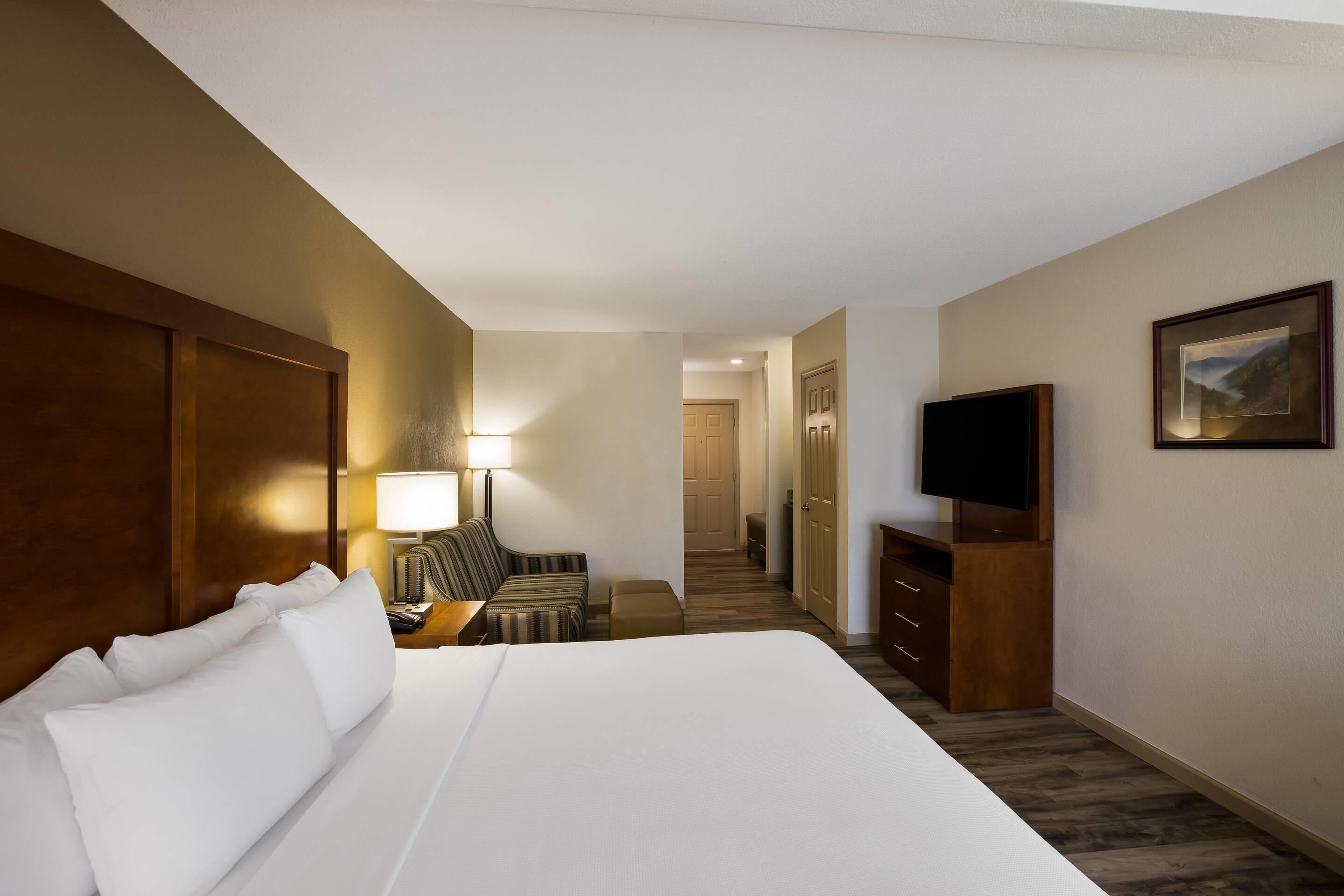 A hotel room with a large bed, a TV, a desk with a lamp, a chair, and a staircase leading to another room.
