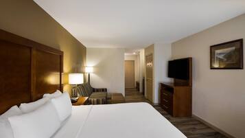 A hotel room with a large bed, a TV, a desk with a lamp, a chair, and a staircase leading to another room.