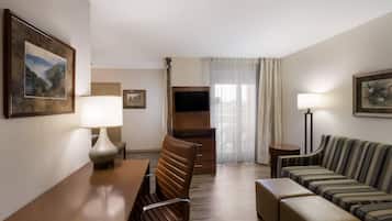 A hotel room with a dining table, a sofa, a TV, and a lamp.