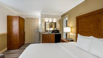 A hotel room with a large bed, a wooden wardrobe, a desk with a lamp, and a mirror above the mirror.