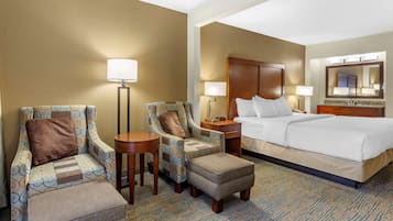 A hotel room with a bed, two armchairs, a small table, a nightstand, and a lamp.