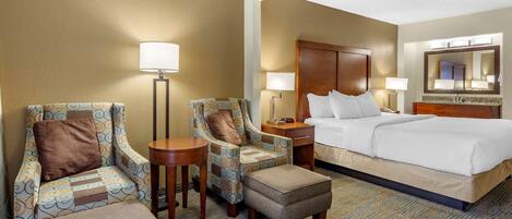 A hotel room with a bed, two armchairs, a small table, a nightstand, and a lamp.