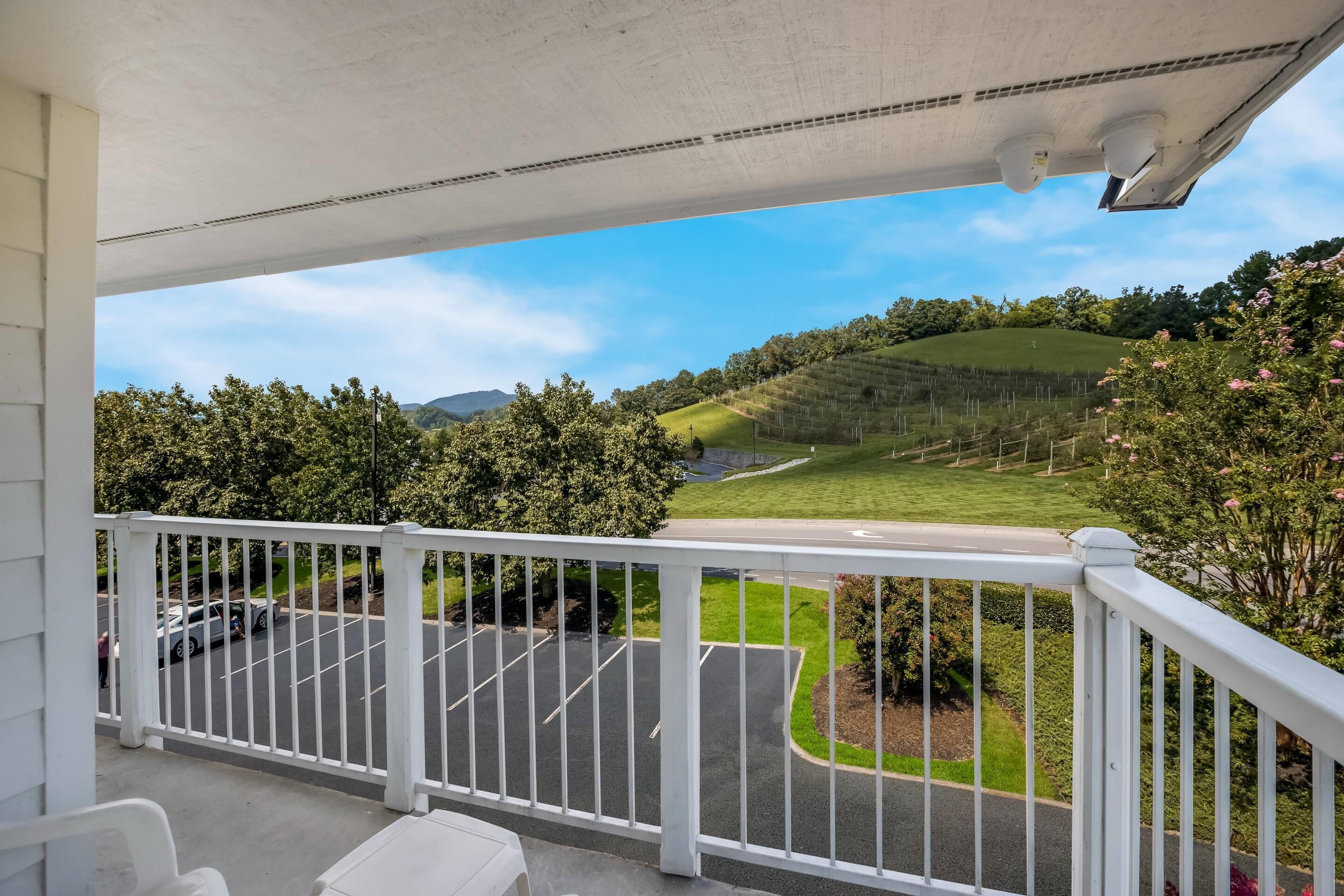 A balcony with a view of a parking lot and green fields.