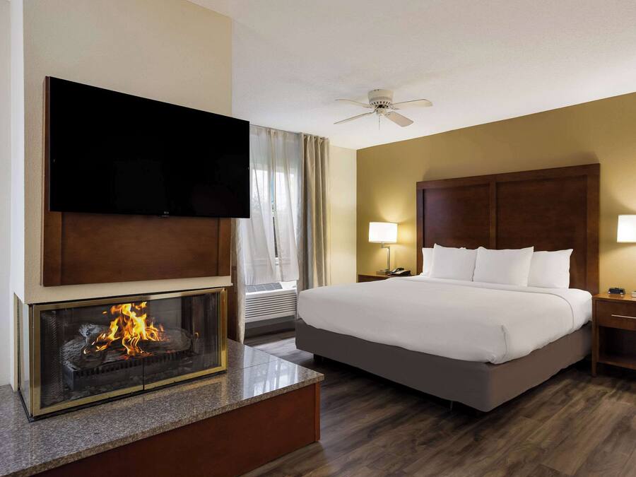 Een hotelkamer met een groot bed, een flatscreen televisie boven een open haard, een plafondventilator en twee bedlampen.
