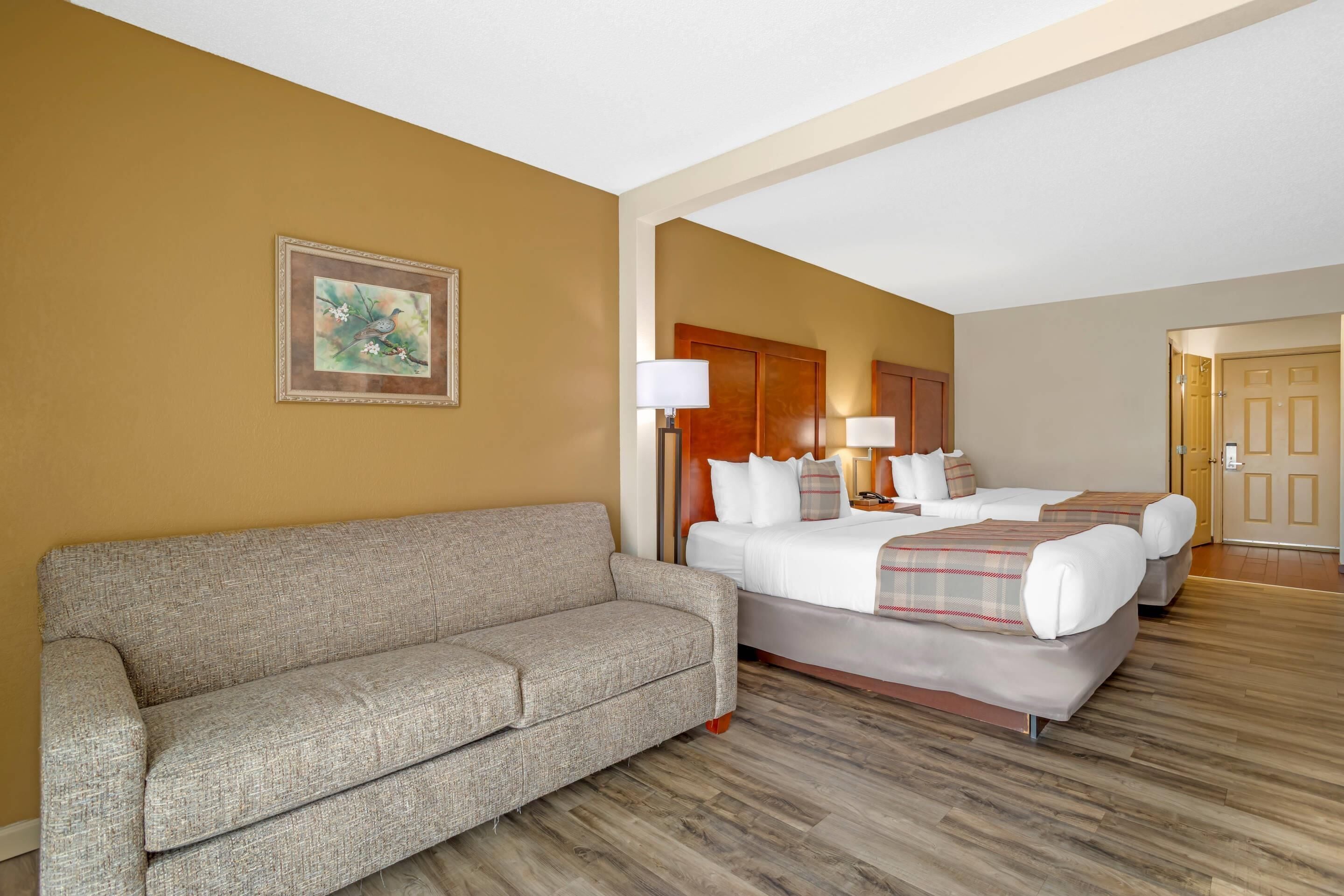 Una habitación de hotel con sofá, cama con manta escocesa y un cuadro en la pared.