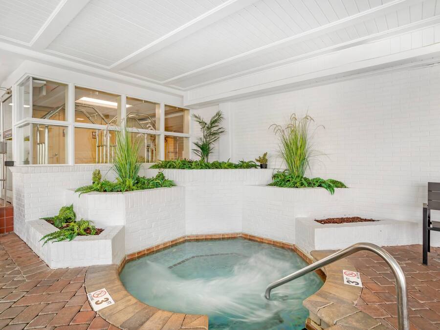 A spa area with a hot tub, white brick walls, and green plants.