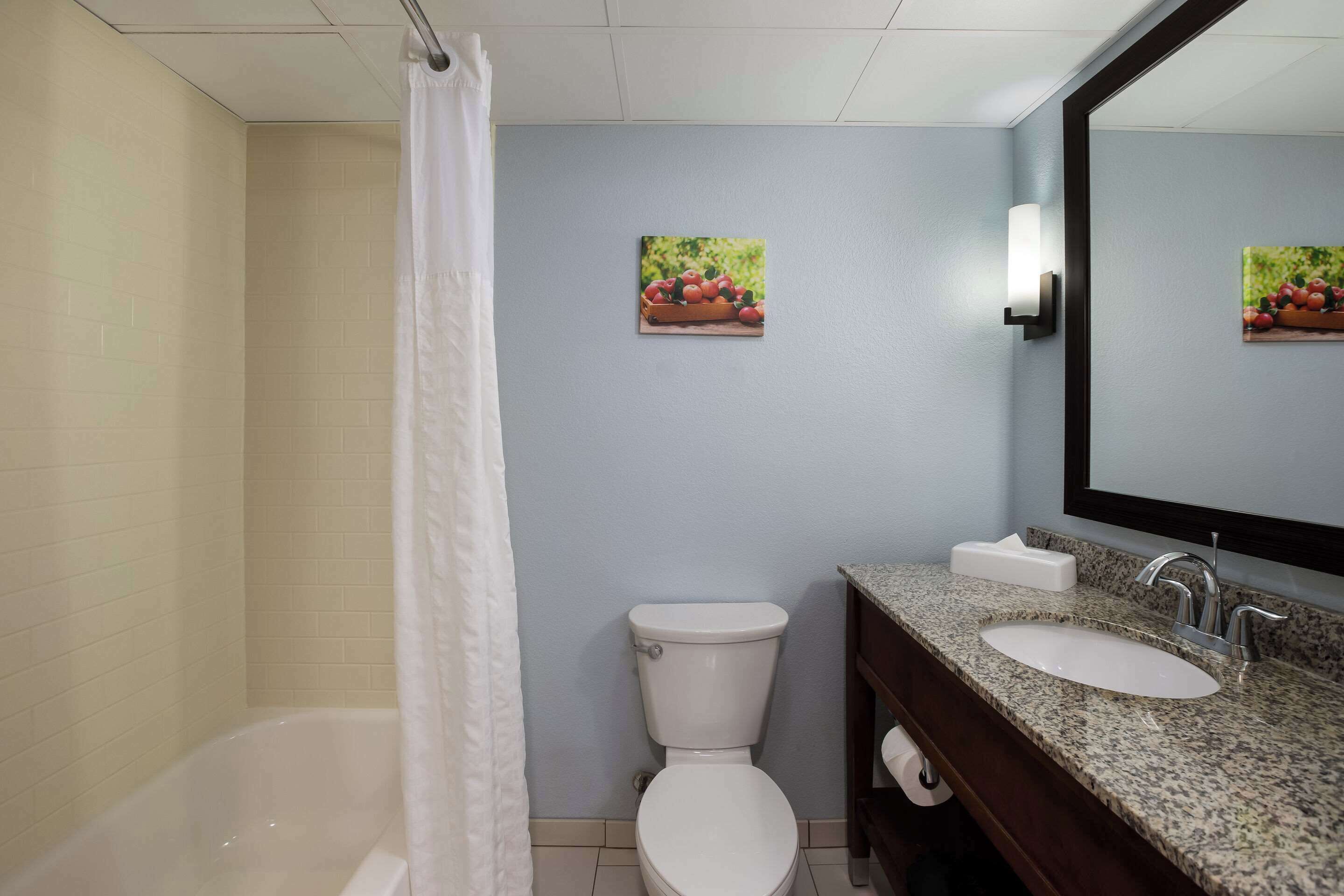 A bathroom with a bathtub, toilet, and sink. There are two wall-mounted light fixtures and two framed pictures of fruit.