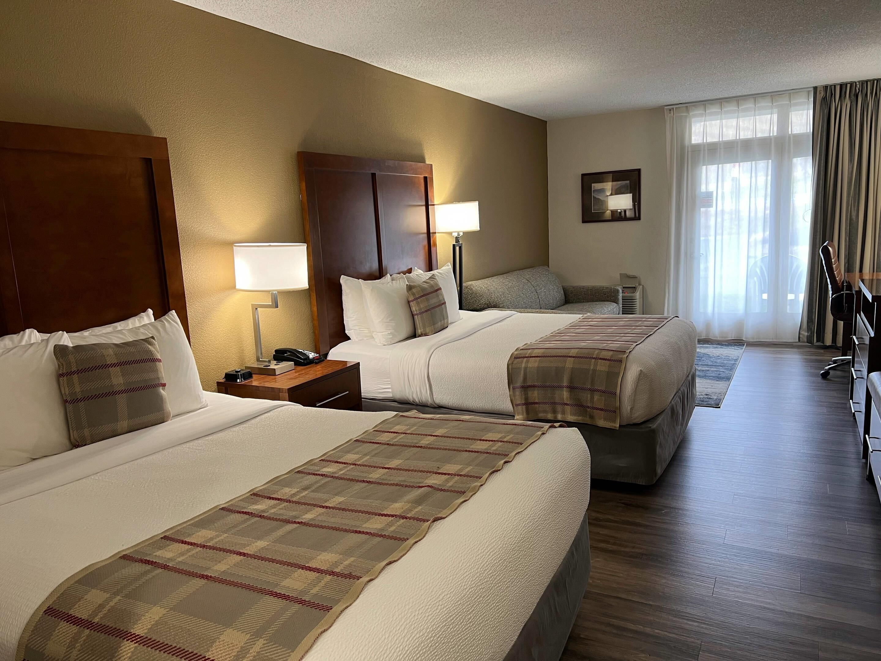 A hotel room with two beds, a desk, a chair, and a window with curtains.