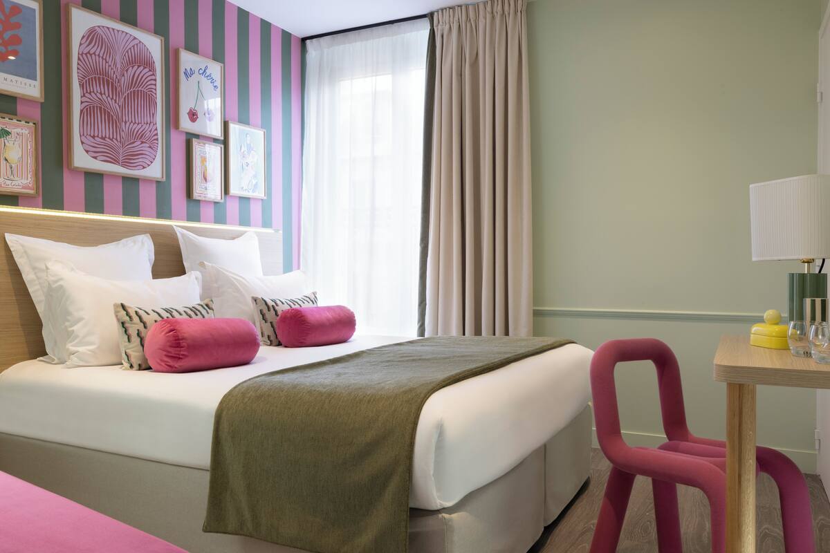 A hotel room with a bed, a desk, a chair, and a window with curtains.
