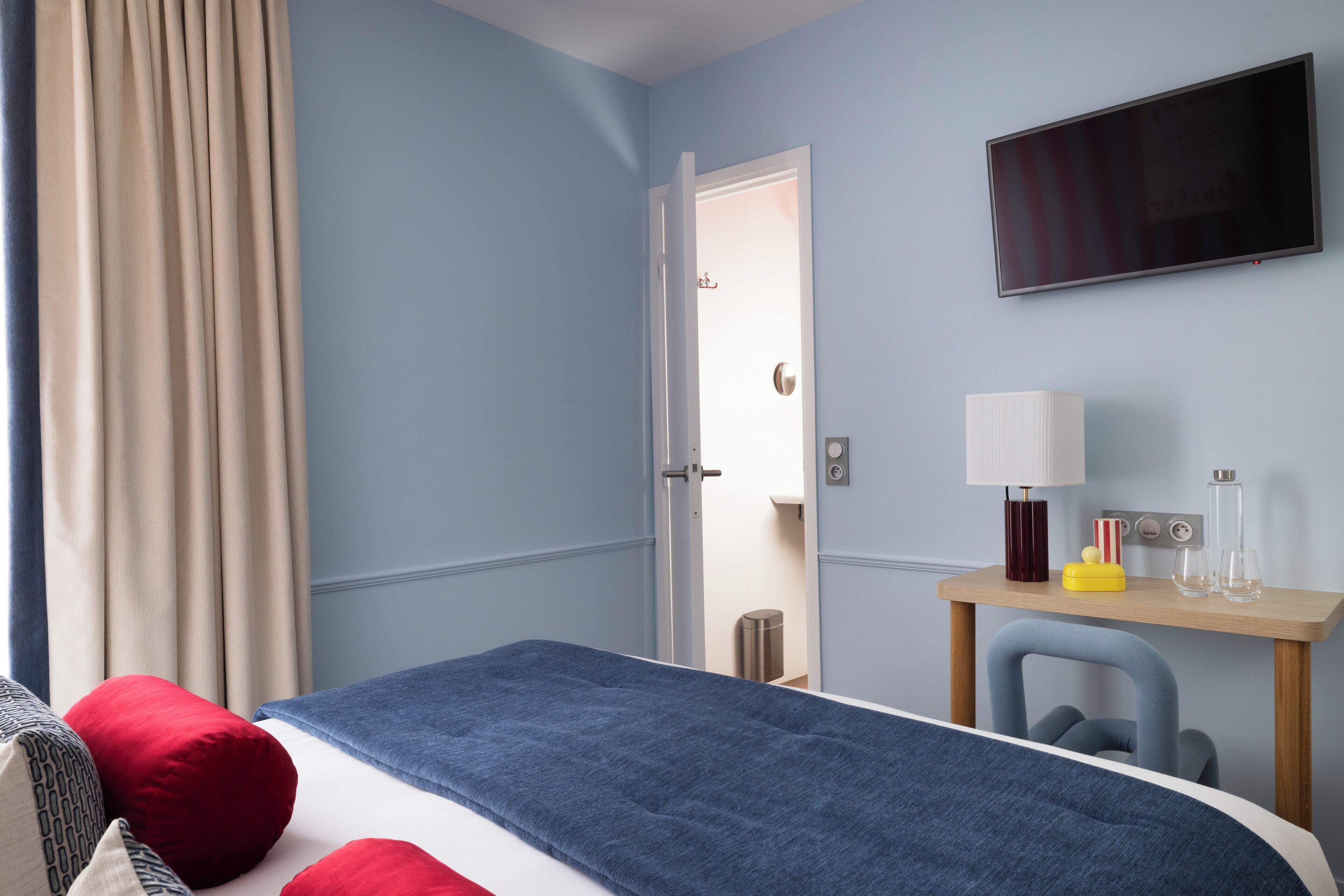 Una habitación de hotel con cama, escritorio, silla, televisor y puerta.