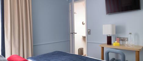 Una habitación de hotel con cama, escritorio, silla, televisor y puerta.