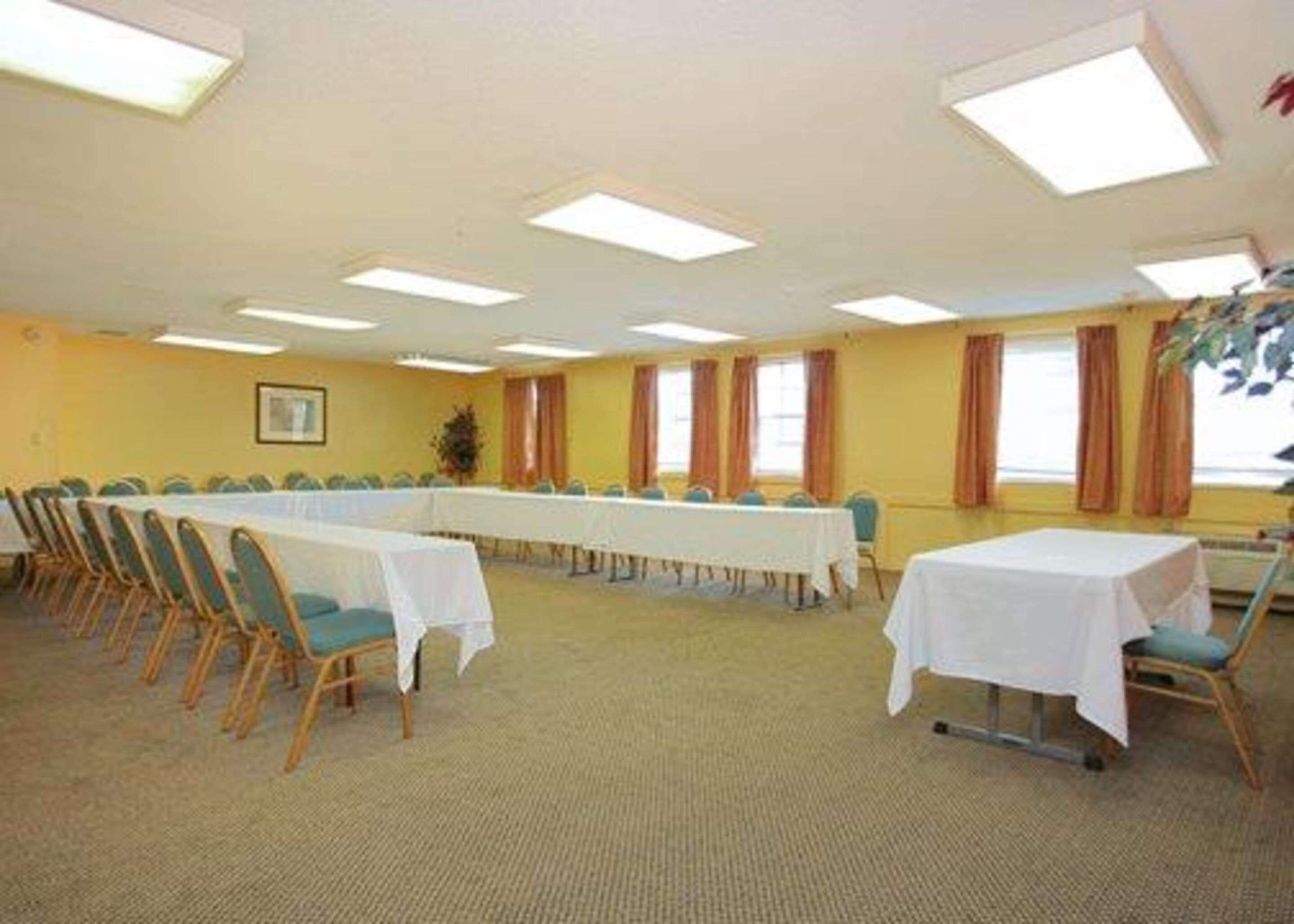 A conference room with a long table, rows of chairs, and large windows with curtains.