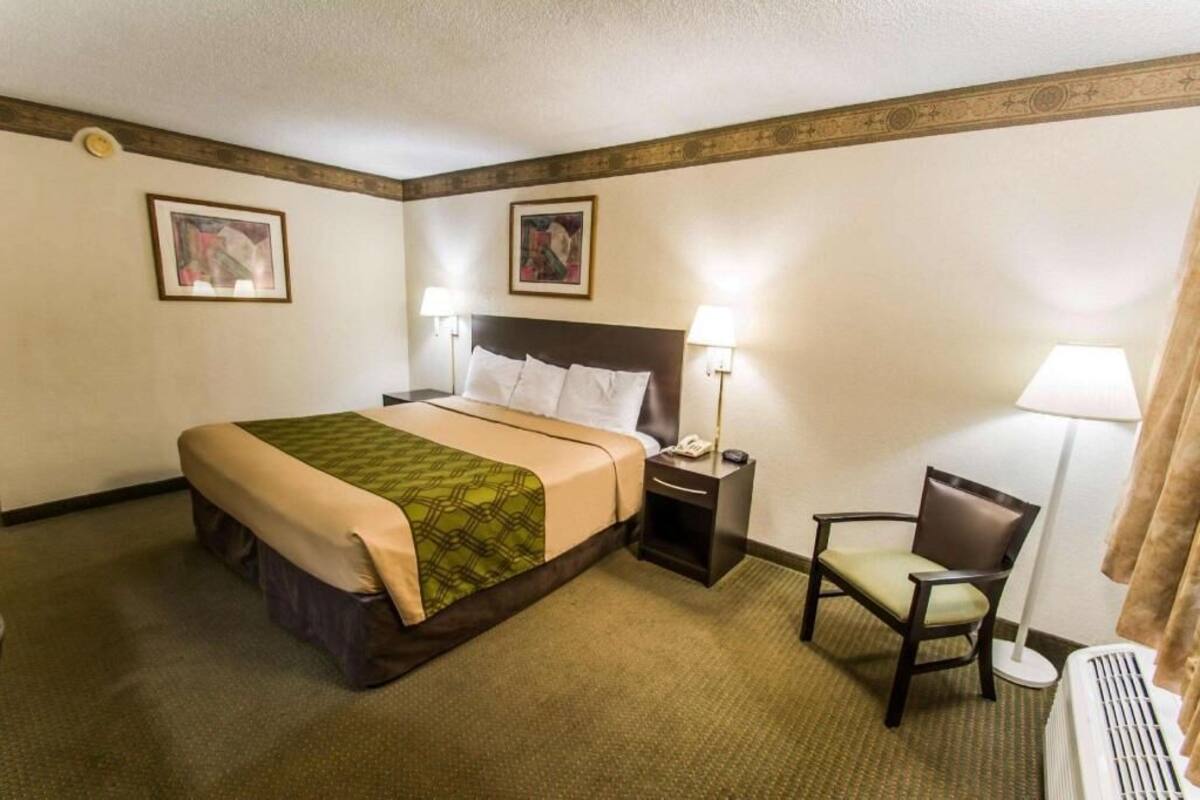 A hotel room with a bed, bedside tables, a chair, and a radiator.