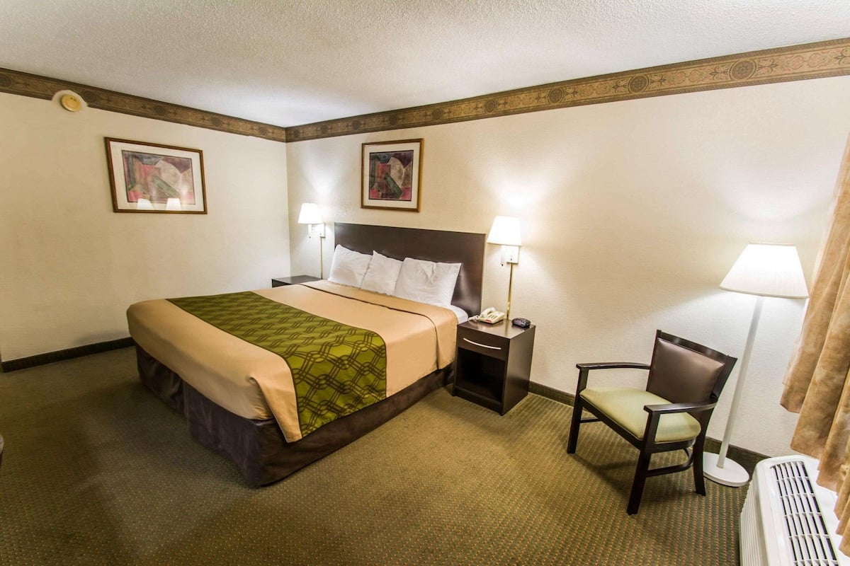 A hotel room with a bed, bedside tables, a chair, and a radiator.