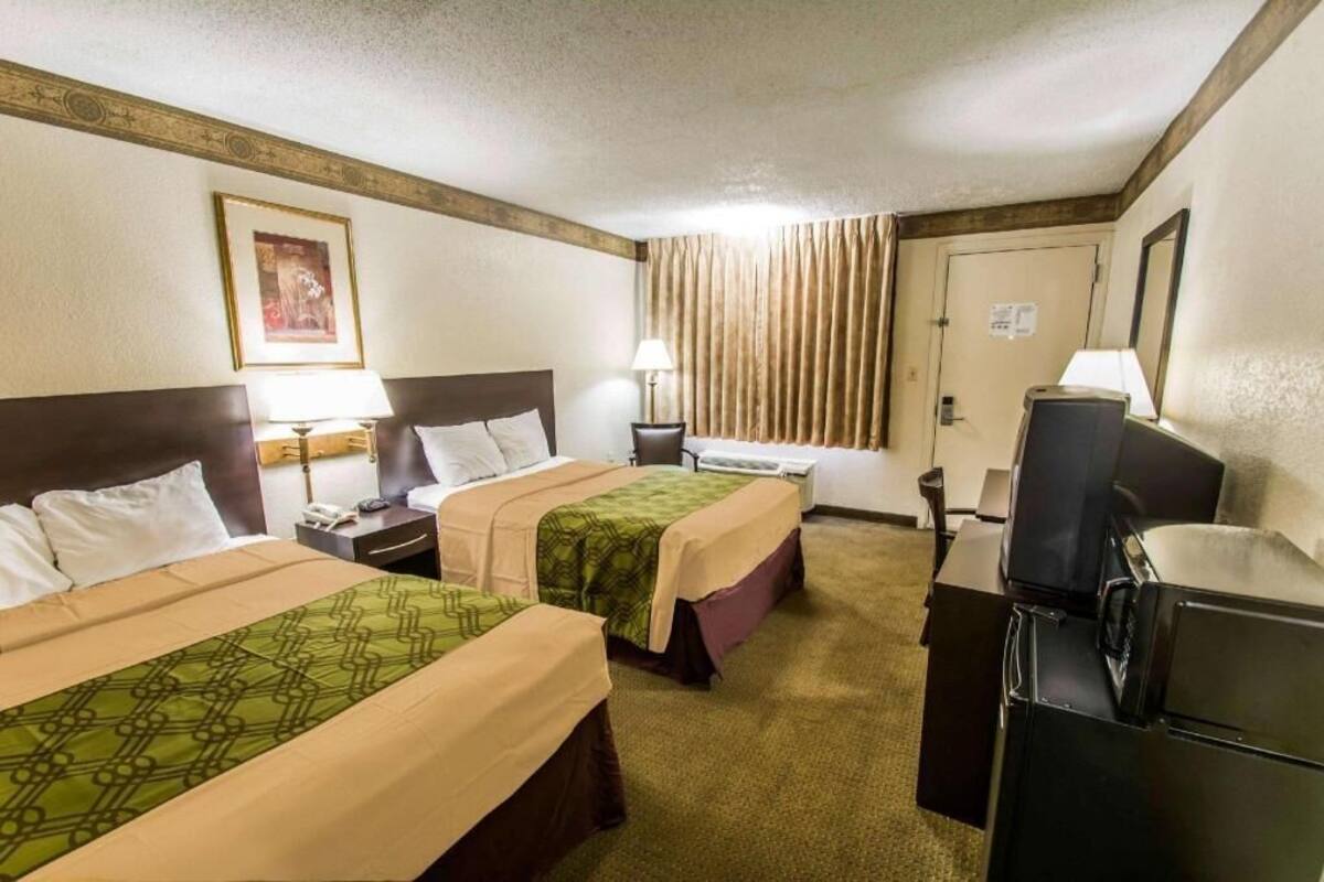 A hotel room with two beds, a desk, a television, and a window with curtains.