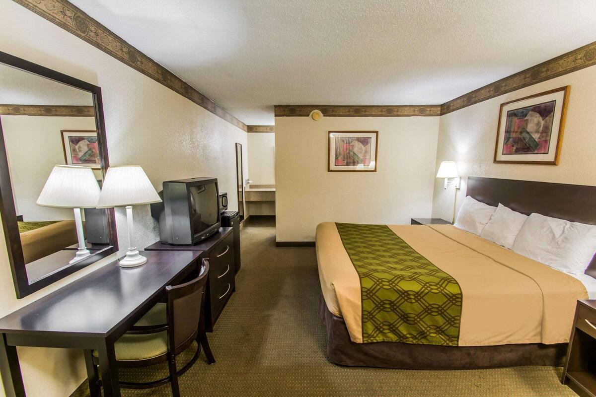 A hotel room with a bed, a desk with a lamp, a television, and a mirror.