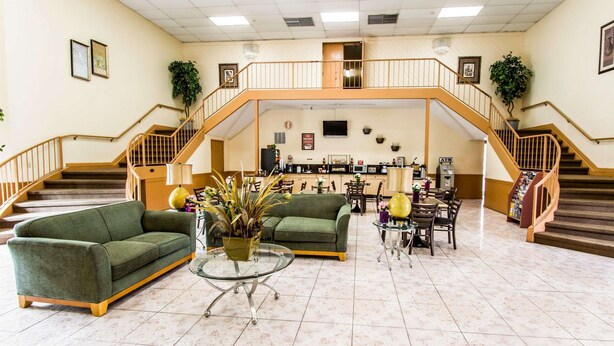 A spacious lobby with a high ceiling, a central staircase, and a seating area with a green sofa and a coffee table.