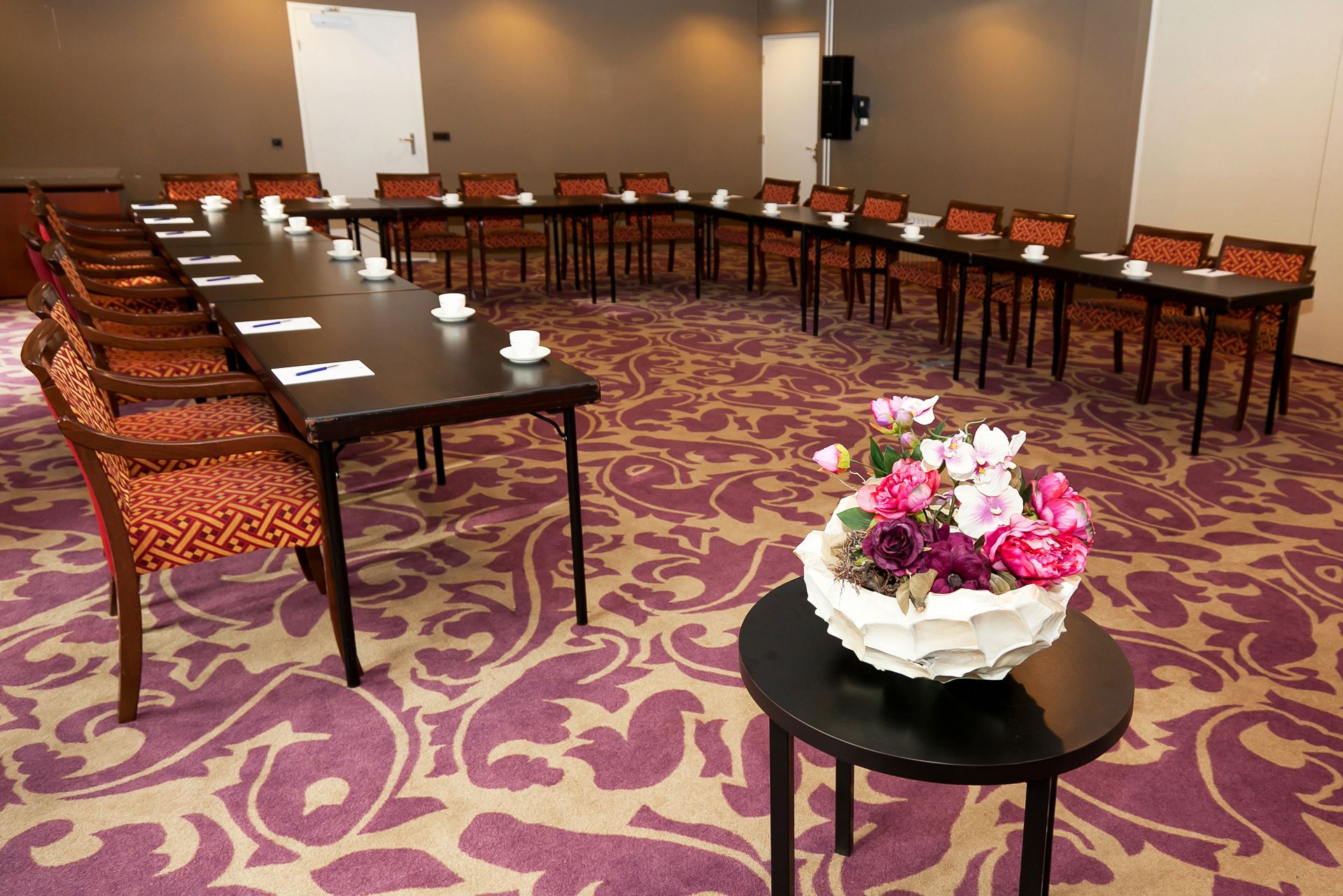 Ein Konferenzraum mit einem langen Tisch, Stühlen, einer floralen Tischdekoration und einem Teppichboden.