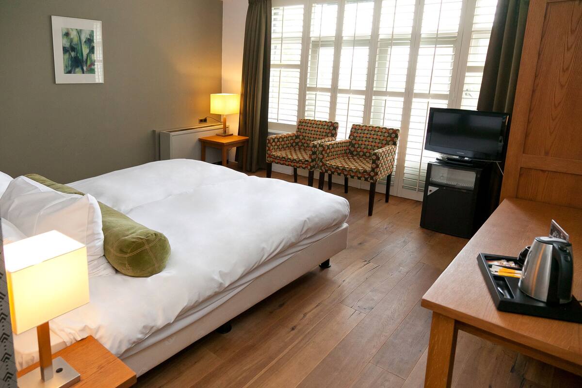 Habitación de hotel con cama, escritorio con televisor, silla y lámpara.