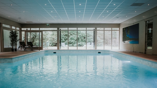 Una piscina interior con paredes de vidrio transparente, suelo de baldosas e iluminación empotrada en el techo.