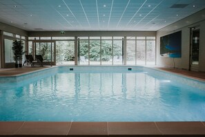 Una piscina interior con paredes de vidrio transparente, suelo de baldosas e iluminación empotrada en el techo.