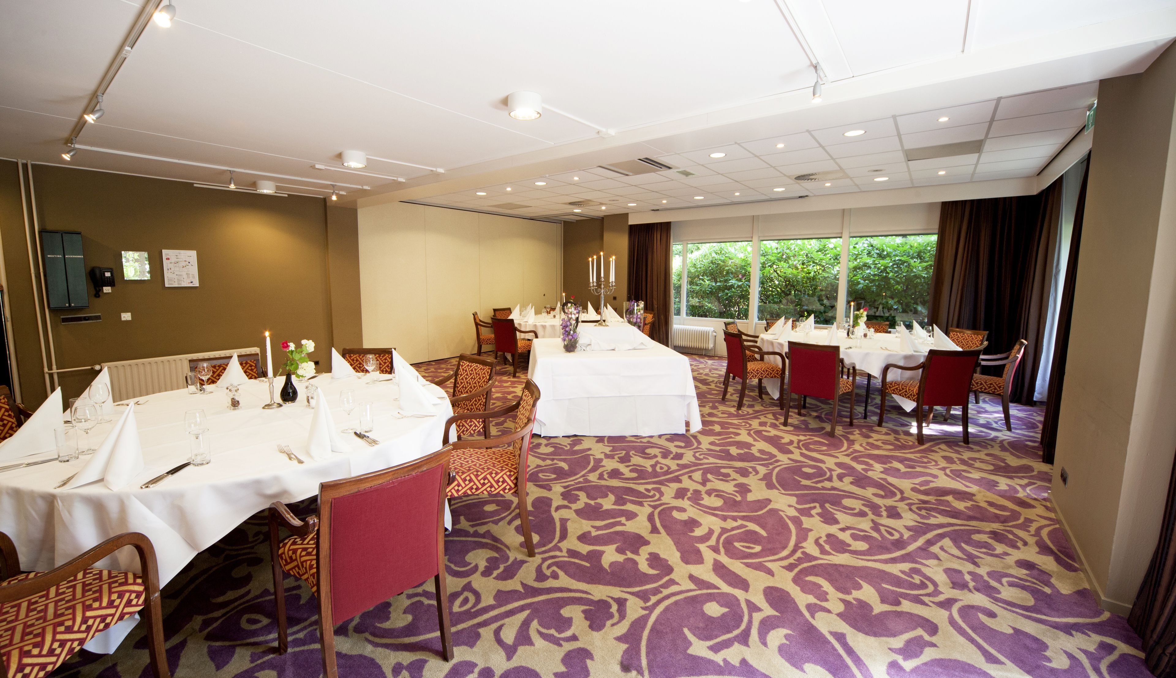 A conference room with multiple tables set for dining, equipped with chairs and a patterned carpet.
