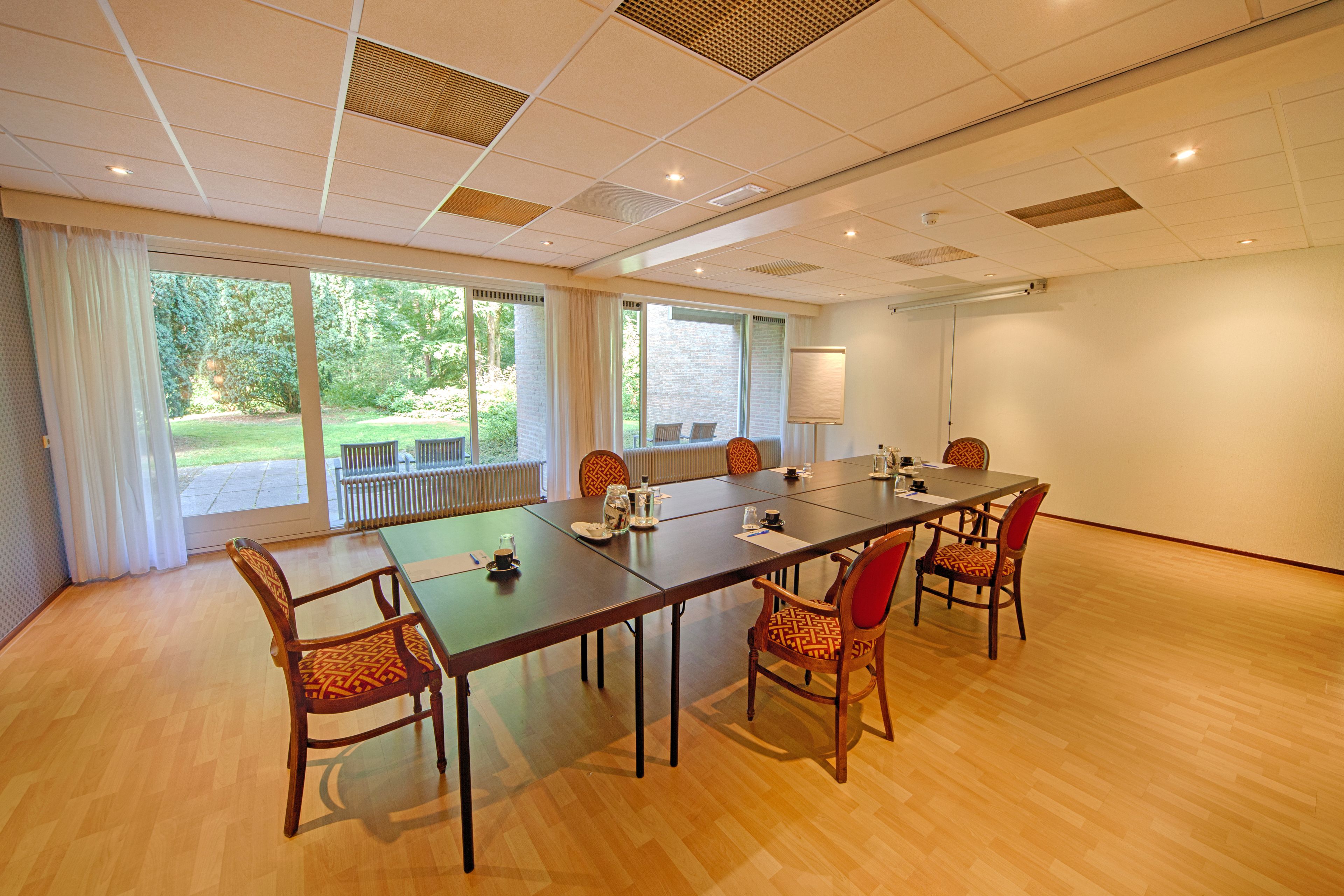Un salón de conferencias con una larga mesa, seis sillas y grandes ventanales con vistas a un jardín.