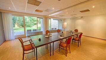Un salón de conferencias con una larga mesa, seis sillas y grandes ventanales con vistas a un jardín.