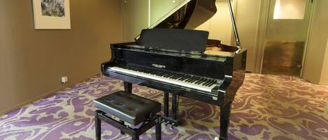 A grand piano in a room with patterned carpet, a bench, and a framed picture on the wall.