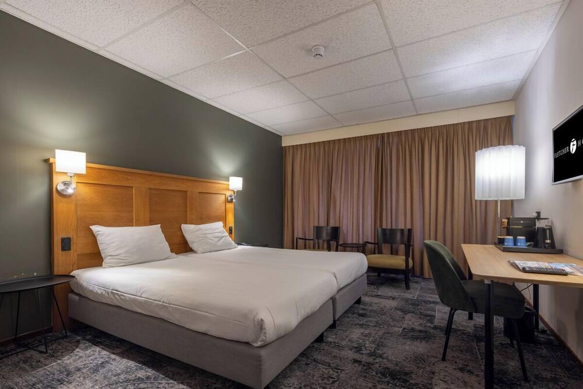 Habitación de hotel con una cama grande, dos mesitas de noche, un escritorio con silla, televisor y ventana con cortinas.