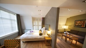 Habitación de hotel con cama, una silla, una mesa, una lámpara y un cuadro en la pared.