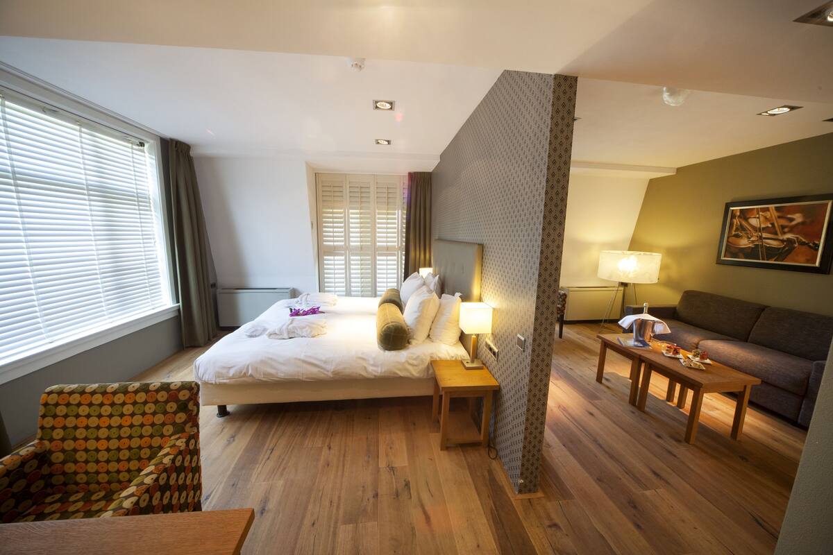 Habitación de hotel con cama, una silla, una mesa, una lámpara y un cuadro en la pared.