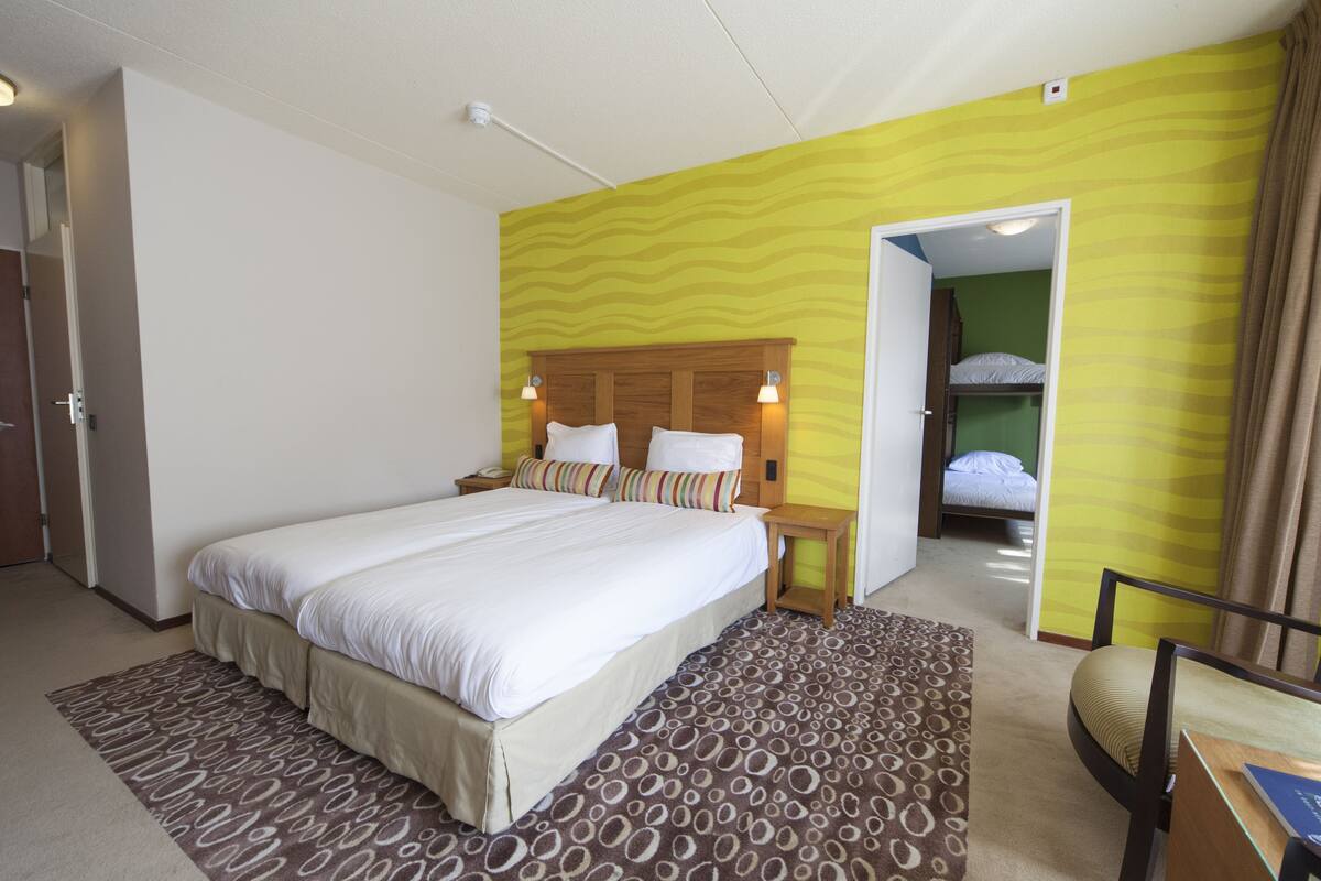 Una habitación de hotel con una cama grande, una mesita de noche, una silla y una litera en la habitación contigua.