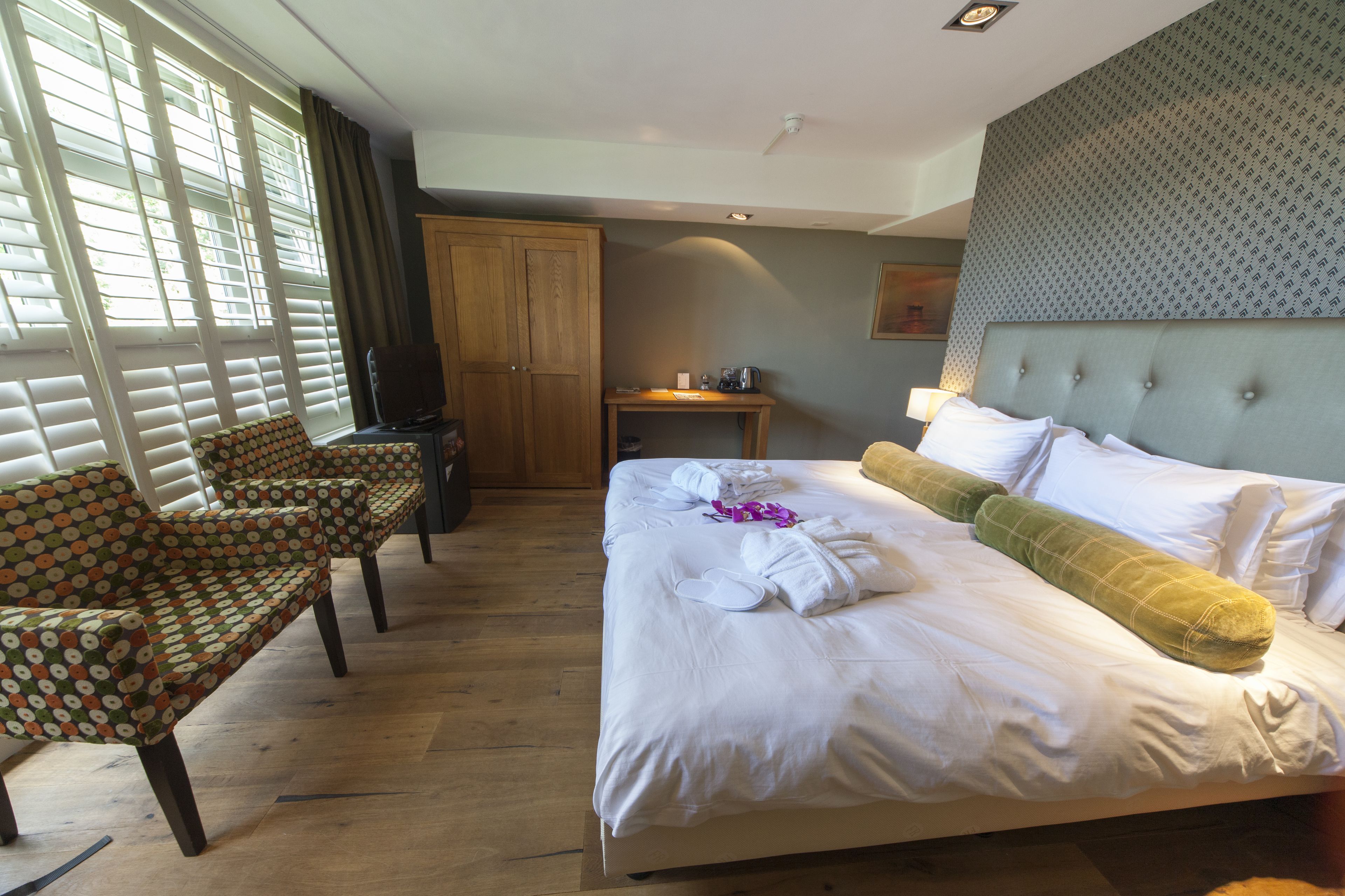 A hotel room with a large bed, a desk, a chair, and a wardrobe.