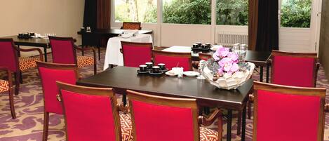 A conference room with a large table, red chairs, and a view of greenery through the windows.