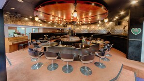 Una zona de bar con un mostrador circular, varios taburetes y un piano al fondo.